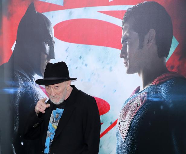 Frank Miller posiert vor Postern von Batman und Superman.