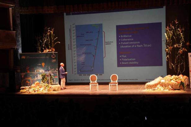 Ein Mann hält einen Vortrag auf einer Bühne, die mit Kürbissen und Maiskolben dekoriert ist.