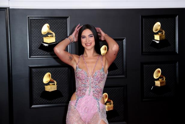 Dua Lipa posiert vor einer Wand mit Grammy-Statuen.