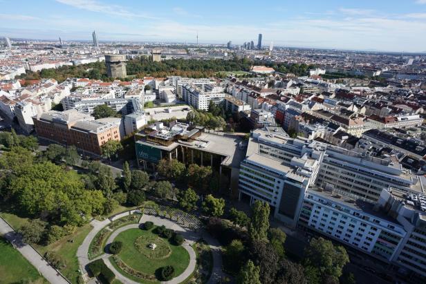 Luftaufnahme von Wien mit Blick auf Gebäude, Parks und den Donauturm am Horizont.