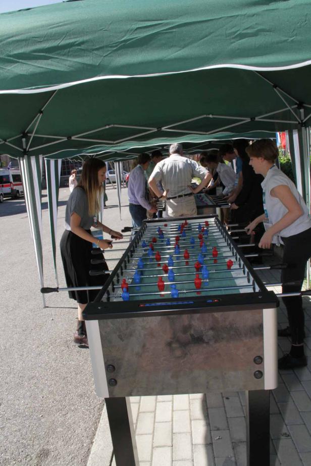 Mehrere Personen spielen an einem Tischfußballspiel unter einem grünen Zelt.