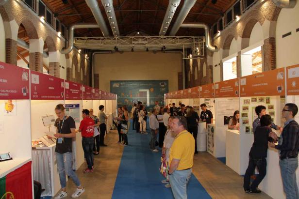 Menschen besuchen eine Ausstellung in einer Halle mit Ständen.