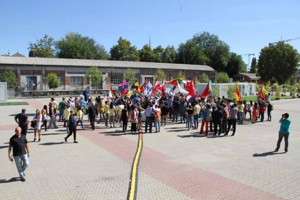 Eine Gruppe von Menschen versammelt sich mit verschiedenen Nationalflaggen auf einem Platz.