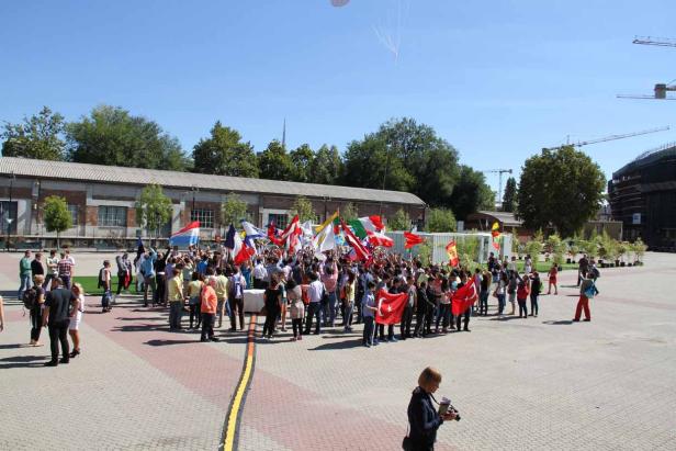 Eine Menschenmenge hält verschiedene Nationalflaggen auf einem Platz hoch.