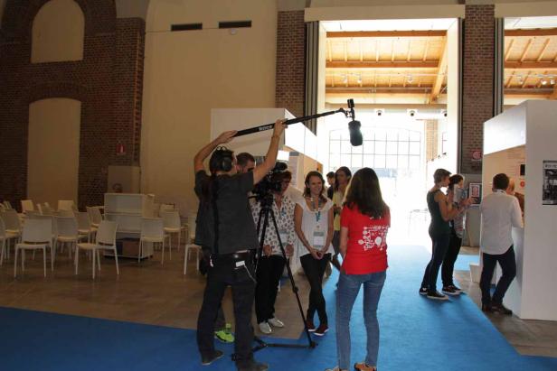 Ein Filmteam interviewt Personen in einer Halle mit Ziegelwänden.