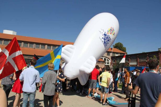 Eine Menschenmenge steht unter einem großen, weißen Werbe-Luftschiff mit Flaggen von Schweden und Dänemark.