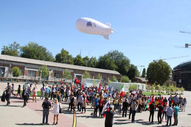 Eine Menschenmenge mit Flaggen verschiedener Länder unter einem Luftschiff.