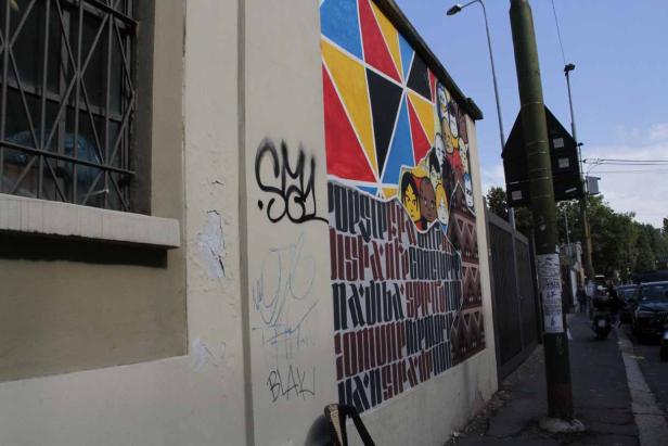 Eine Wandmalerei mit bunten geometrischen Formen und stilisierten Gesichtern an einer Hauswand.