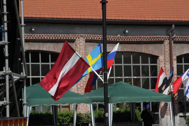 Mehrere Flaggen, darunter Lettlands, Schwedens und Russlands, wehen vor einem Gebäude.