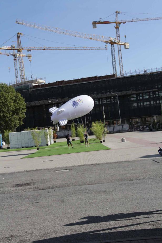 Zwei Männer halten einen großen, weißen Werbezeppelin auf einem Platz.