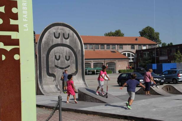 Kinder spielen auf einem Platz mit einer Rampe und einer großen Skulptur mit einem Smiley-Gesicht.