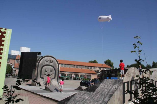 Kinder spielen auf einem Skatepark mit einem Luftschiff im Hintergrund.