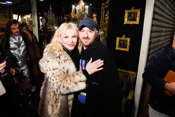 Courtney Love und ein Mann posieren für ein Foto vor einem dekorierten Hintergrund.