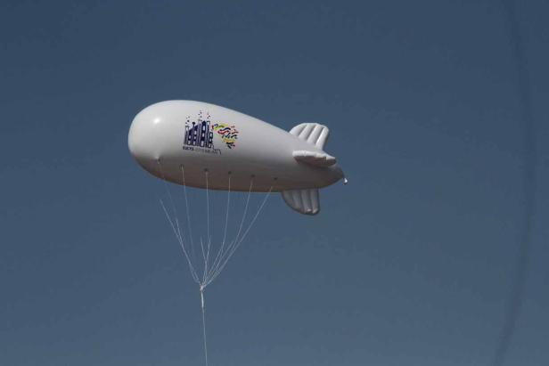 Ein weißer Zeppelin mit der Aufschrift „EUCYS 2015 Milan“ vor blauem Himmel.