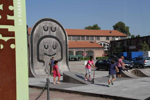 Kinder spielen auf einem Skatepark mit einer großen Betonwand mit einem Smiley-Gesicht.