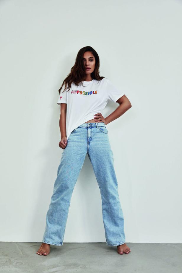 Eine Frau posiert barfuß in Jeans und einem T-Shirt mit der Aufschrift „I'm Possible“.