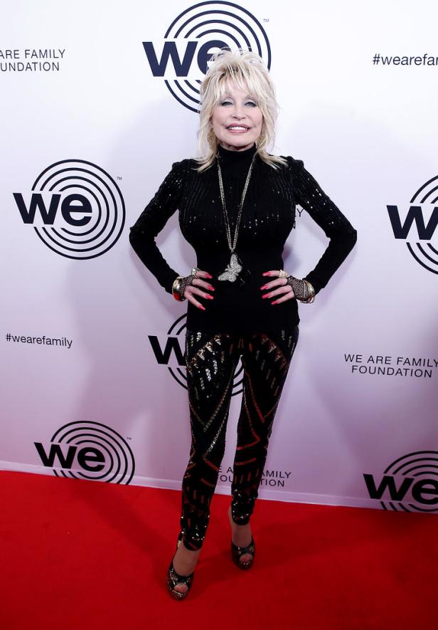 Dolly Parton posiert auf einem roten Teppich vor dem Hintergrund des „We Are Family“-Logos.