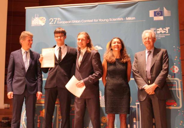 Eine Gruppe von Personen posiert vor einem Banner des 27. Europäischen Wettbewerbs für junge Wissenschaftler in Mailand.