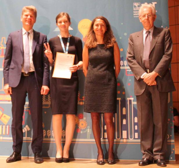 Vier Personen posieren vor einem Banner bei einer Preisverleihung.