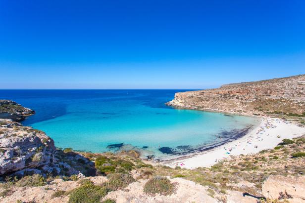 Blick auf einen Strand mit türkisfarbenem Wasser und vielen Badegästen.