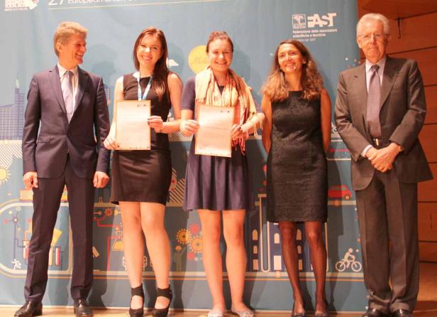 Fünf Personen stehen auf einer Bühne und halten Urkunden in den Händen.