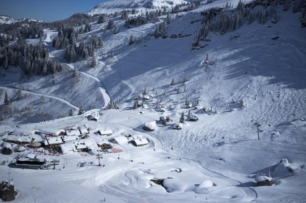Blick auf ein verschneites Bergdorf mit Skipisten und bewaldeten Hängen.