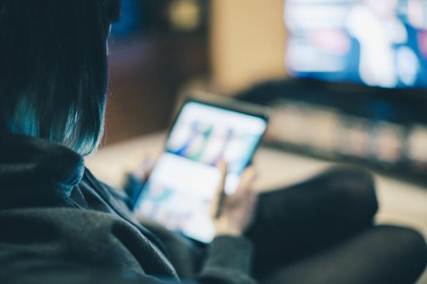 Eine Frau sitzt mit einem Tablet auf der Couch.