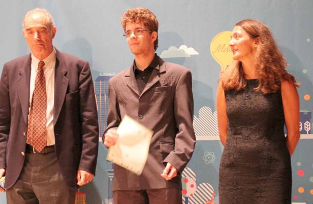 Drei Personen stehen vor einem farbenfrohen Hintergrund bei einer Preisverleihung.