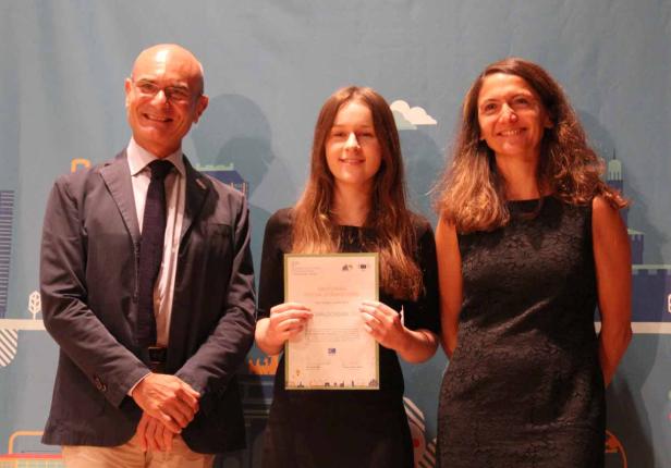 Eine junge Frau hält eine Urkunde zwischen zwei Personen.