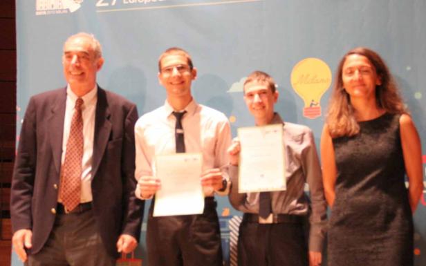 Vier Personen posieren mit Urkunden vor einem hellblauen Hintergrund.