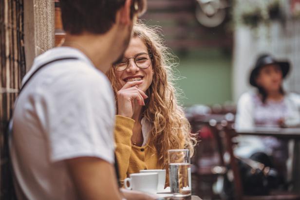 Eine lächelnde Frau mit Brille sitzt mit einem Mann in einem Café.
