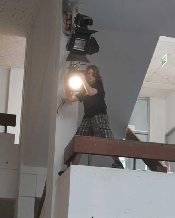 Eine Person justiert eine helle Bühnenlampe, die an einer Wand montiert ist.