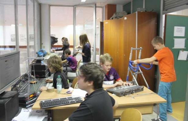 Eine Gruppe von Jugendlichen arbeitet in einem Raum mit Computern und technischer Ausrüstung.