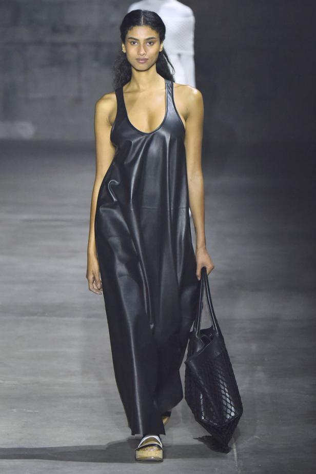 Eine Frau in einem schwarzen Lederkleid mit einer passenden Handtasche auf einem Laufsteg.
