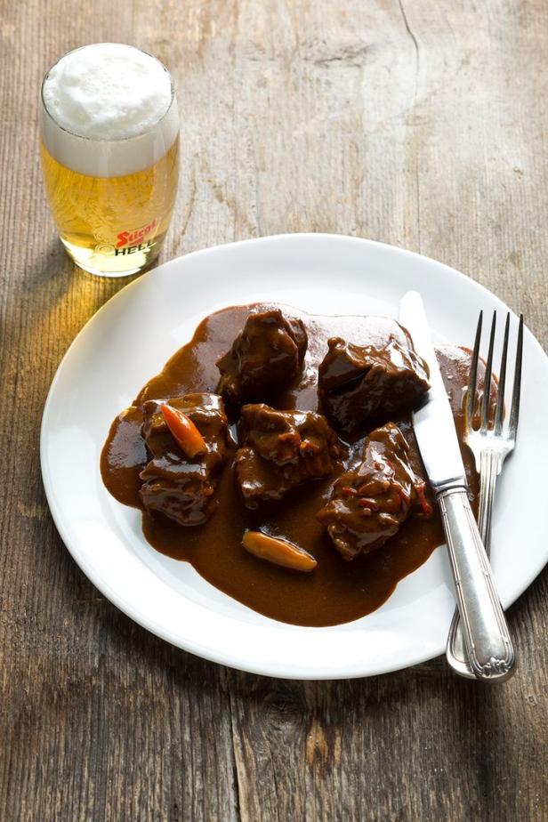 Ein Teller mit Rindfleisch in dunkler Soße, dazu ein Glas Bier.