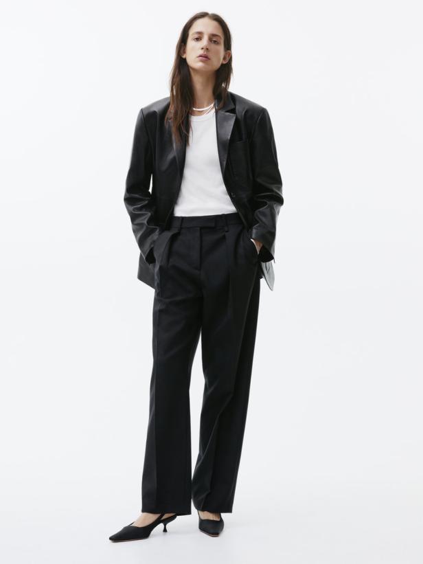 Eine Frau trägt einen schwarzen Blazer, ein weißes T-Shirt und eine schwarze Hose.