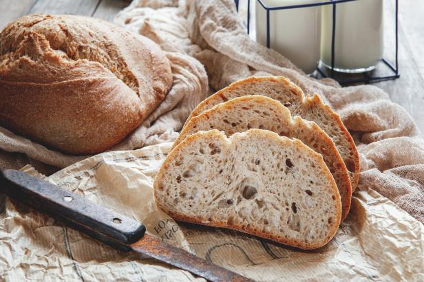Ein Laib Brot und drei Scheiben Brot liegen auf Packpapier mit einem Messer.