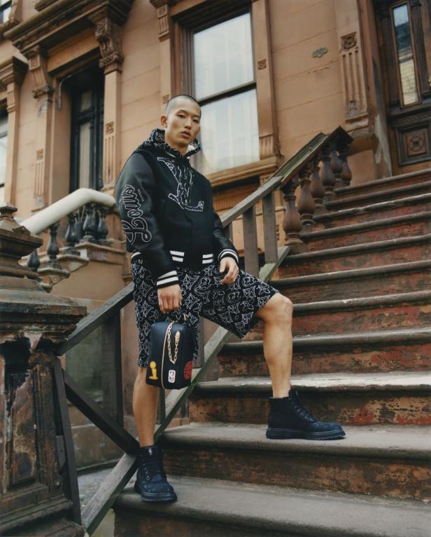 Ein Mann in einer Louis Vuitton Jacke und Shorts steht auf einer Treppe vor einem Gebäude.