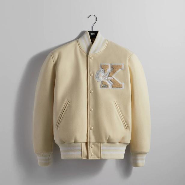 Eine hellgelbe Collegejacke mit einem großen „K“-Logo und einem geflügelten Einhorn darauf.