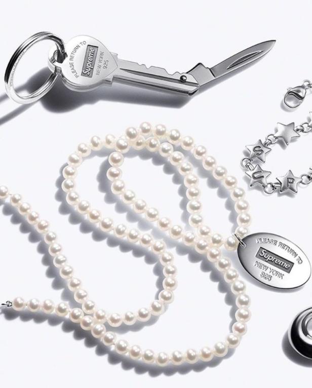 Eine Perlenkette, ein Schlüsselanhänger mit Messer und ein Armband mit Sternen von Supreme liegen auf einem weißen Hintergrund.