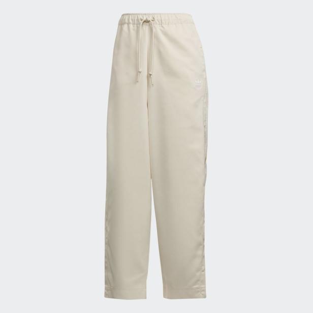 Eine hellbeige Adidas-Hose mit weitem Bein und seitlichen Knöpfen.
