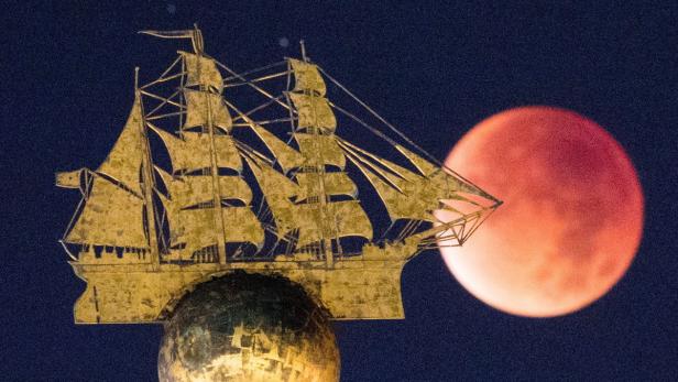 Eine goldene Schiffsstatue vor einer blutroten Mondfinsternis.