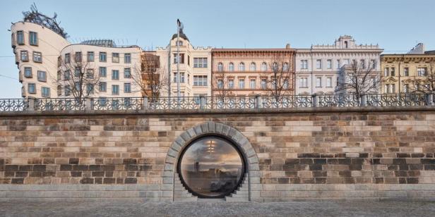 Das tanzende Haus und andere Gebäude in Prag, gesehen durch ein rundes Fenster in einer Mauer.