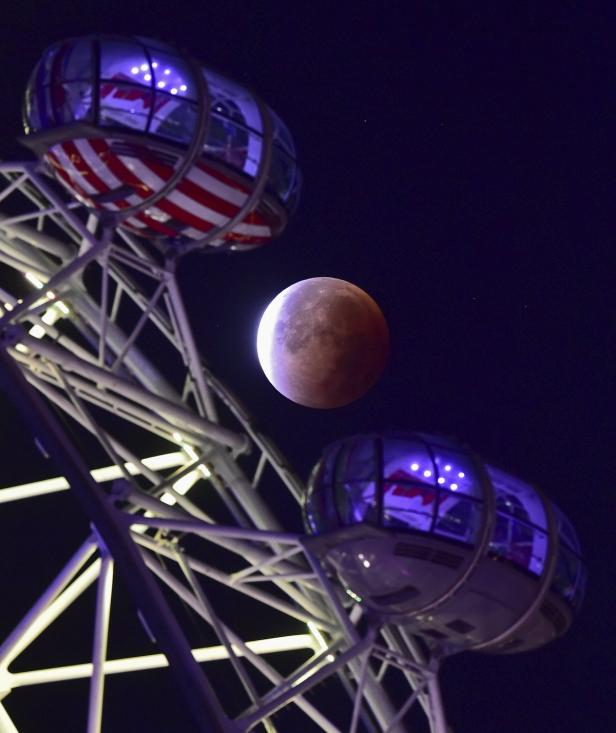 Eine Mondfinsternis, gesehen durch das Riesenrad mit beleuchteten Gondeln.