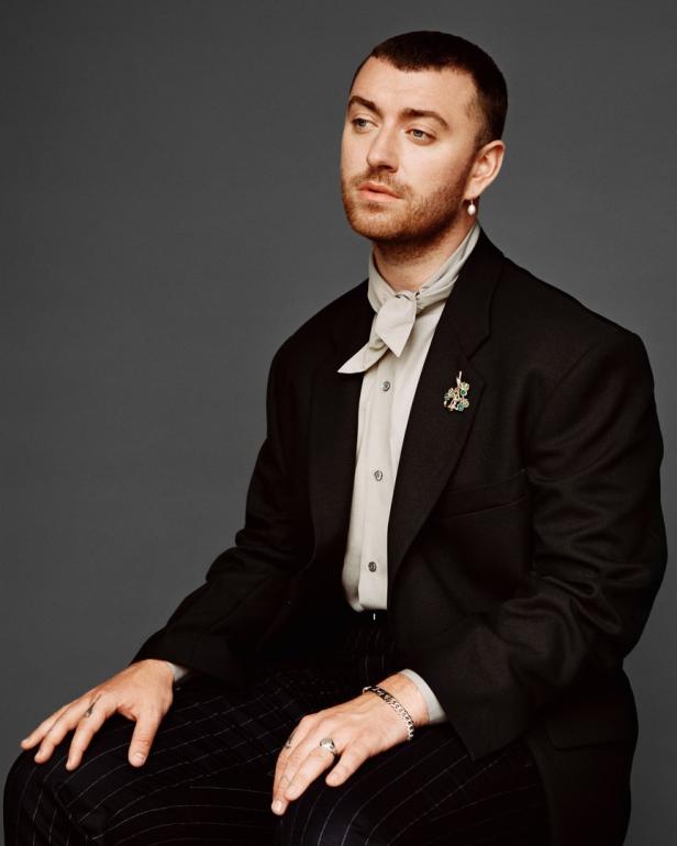 Sam Smith sitzt in einem schwarzen Anzug und blickt nach links.