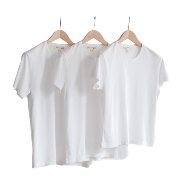 Drei weiße T-Shirts hängen an hellbraunen Holzbügeln vor einem weißen Hintergrund.