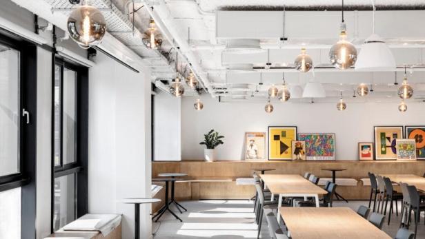 Ein heller Büroraum mit Holztischen, Stühlen und dekorativen Lampen.