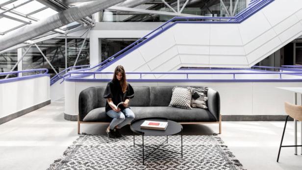 Eine Frau liest ein Buch auf einem Sofa in einem modernen Gebäude.