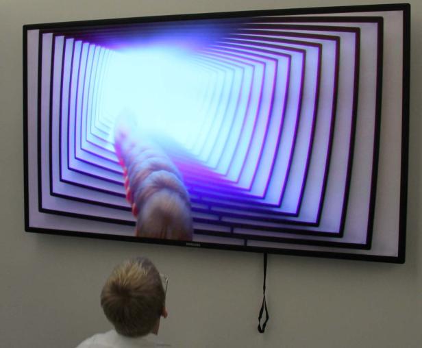 Eine Person betrachtet einen Fernseher mit einer abstrakten Tunneldarstellung.