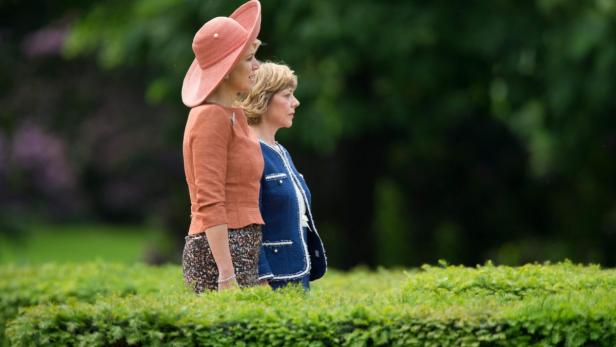 Zwei Frauen stehen in einem Garten, eine mit einem großen, pfirsichfarbenen Hut.